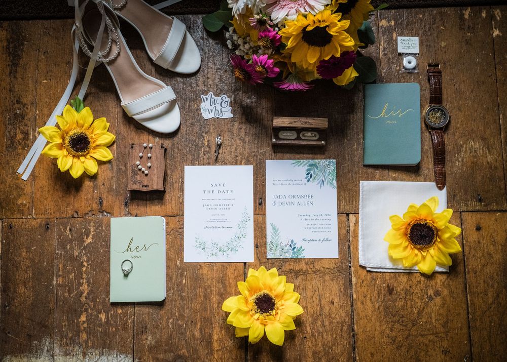 Flat lay of sunflower wedding details including invitations, rings, heels, and bouquet.
