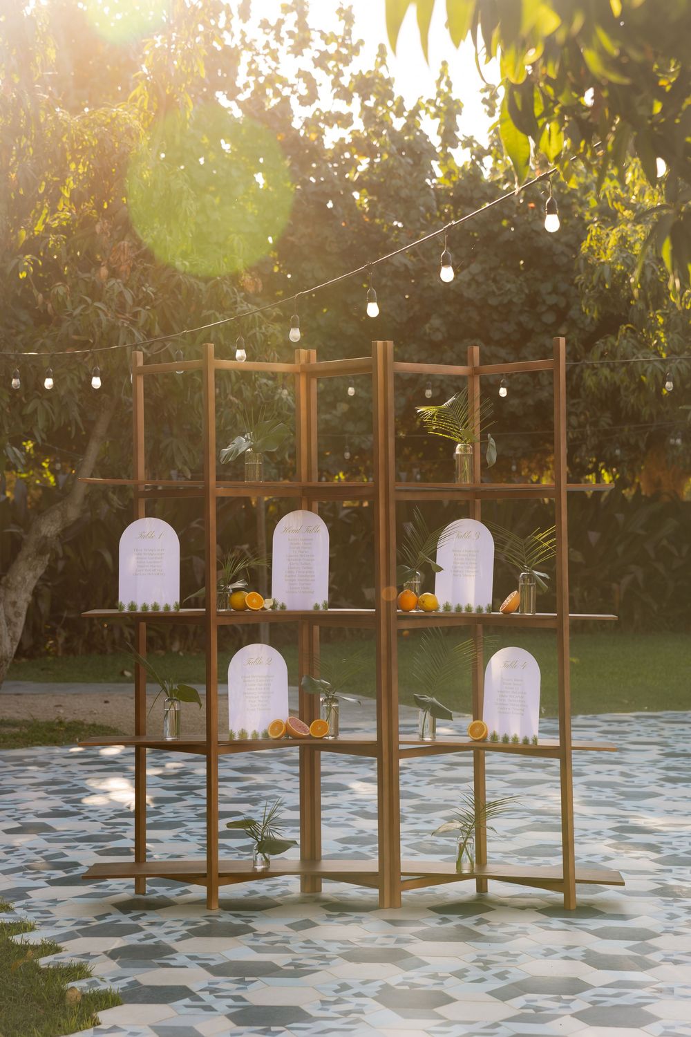 Rustic wooden shelving display with white arch cards and orange floral accents at golden hour outdoor wedding reception.
