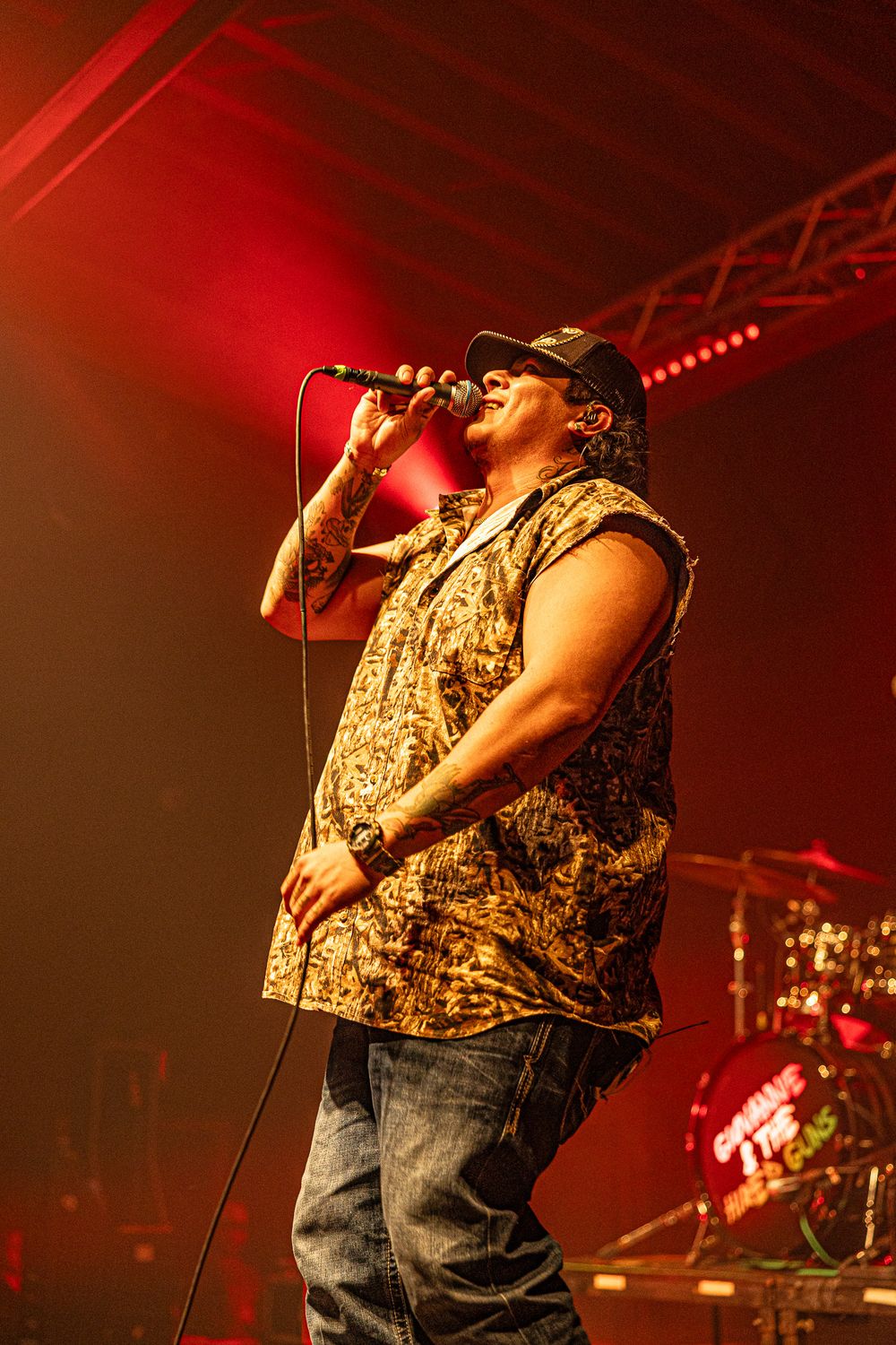 Male vocalist in floral sleeveless shirt sings passionately under red stage lights.