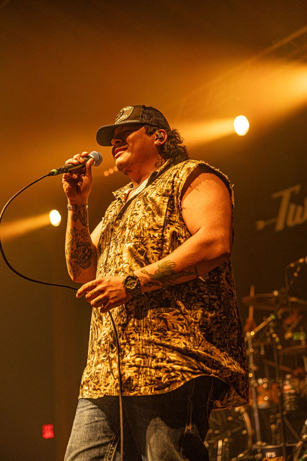 Tattooed male singer in floral shirt performs under warm golden stage lighting.