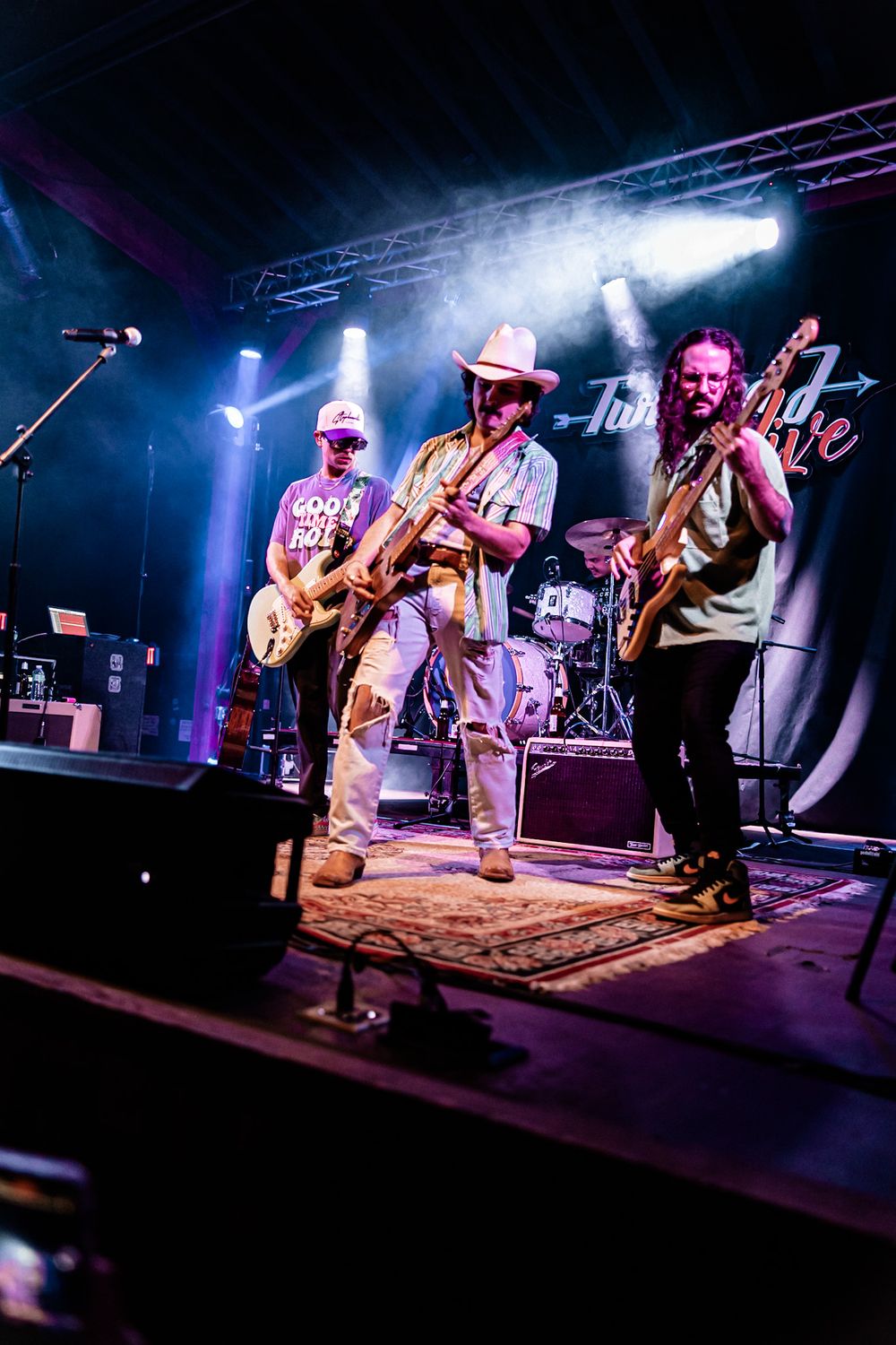 Three guitarists perform energetically on a lit stage at Twisted Love venue.