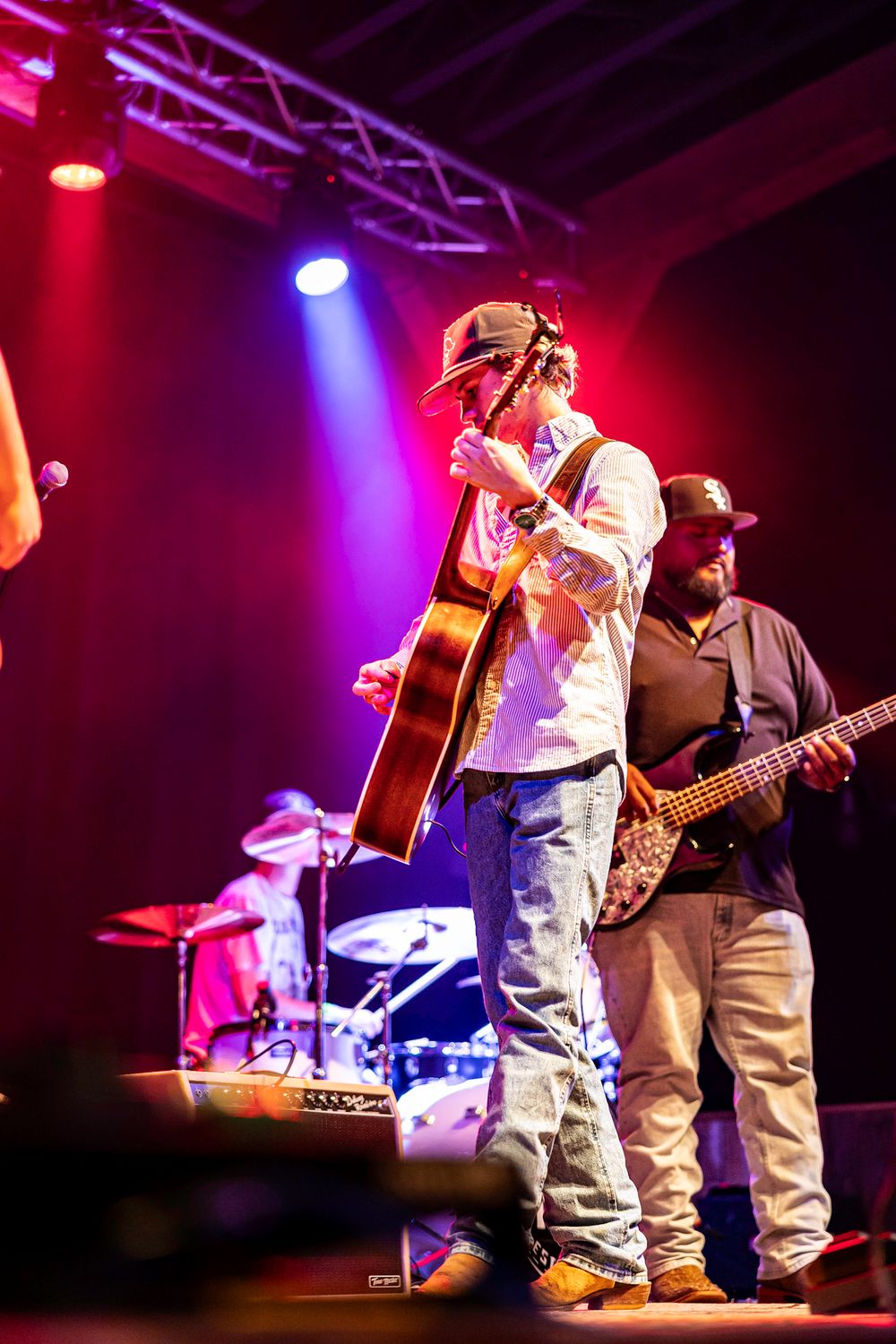 Guitarist plays acoustic guitar on stage under purple and red concert lighting.