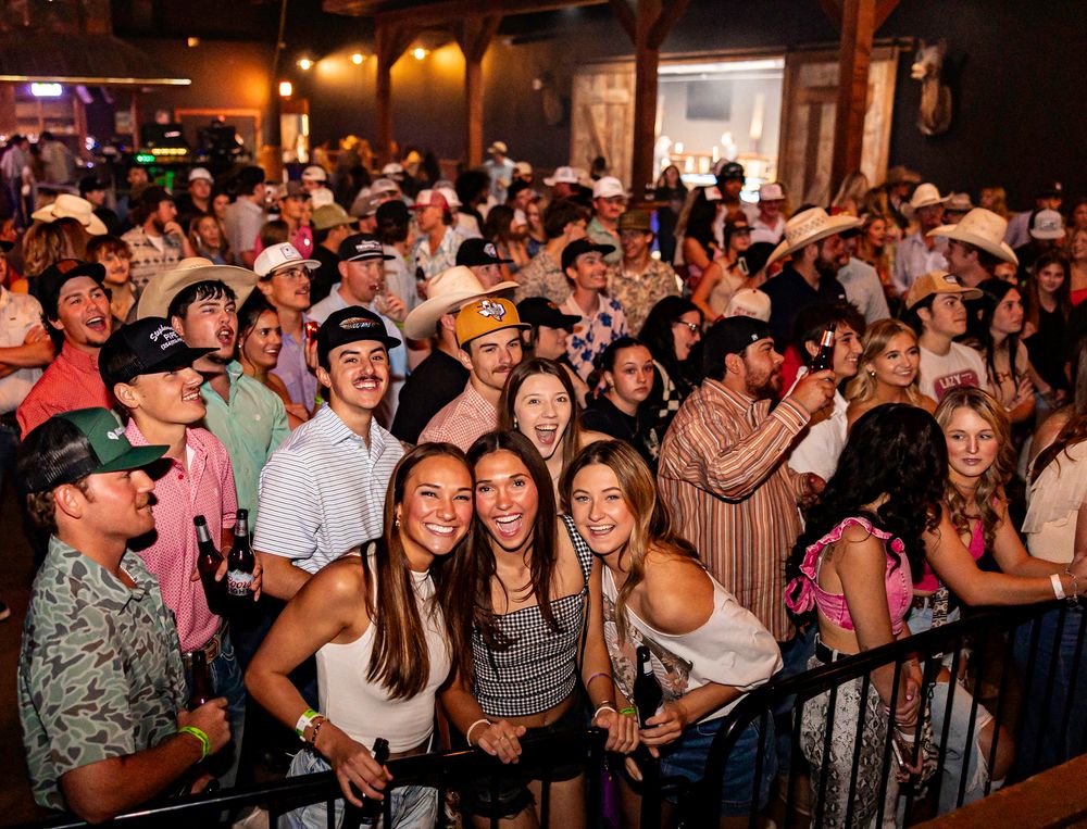 Large crowd of fans in cowboy hats smile at a lively indoor concert venue.