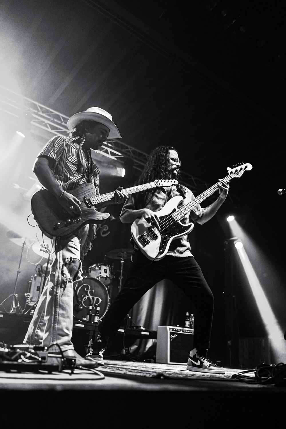 Two guitarists perform intensely on stage in dramatic black and white concert photo.