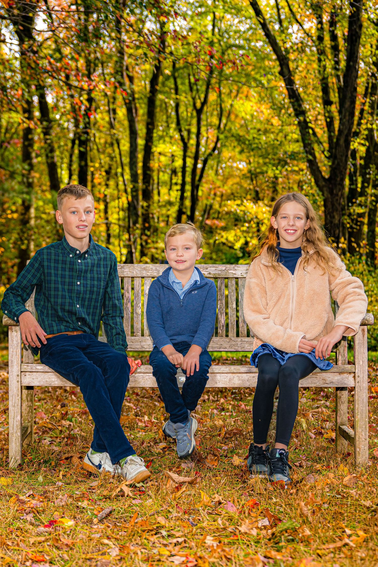 Family of four smiling together on a stone wall at sunset with a vibrant orange sky backdrop.