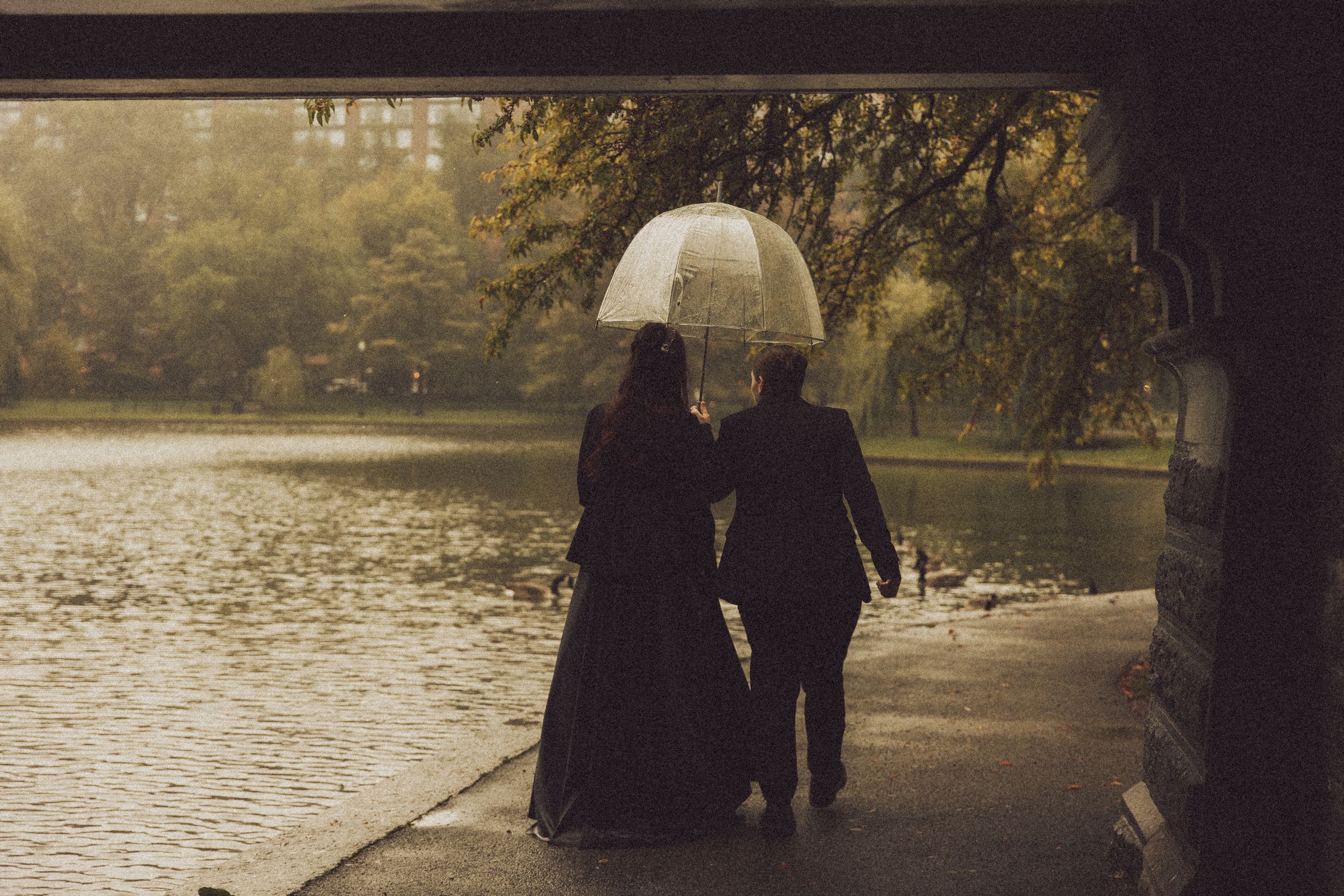 Couple walking under a clear umbrella in the rain near a misty lake surrounded by autumn trees.