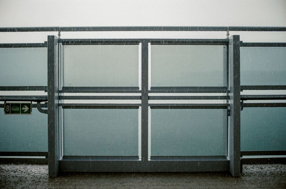 A modern metal gate with frosted glass panels and a green exit sign, set against a grey overcast sky.