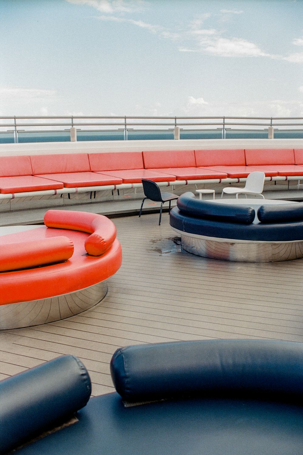 Colorful red and navy blue curved lounge seating on a cruise ship deck overlooking the ocean.