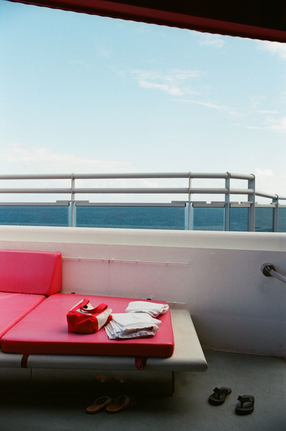 Pink bench seat with red bag and folded items on ferry deck overlooking calm blue ocean horizon.