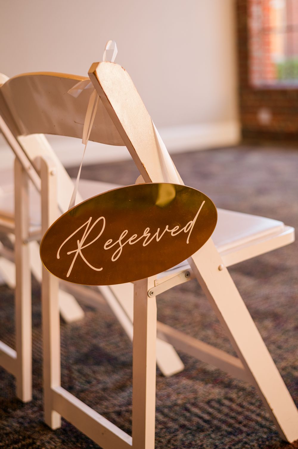 Gold oval Reserved sign hanging on a white folding chair at an elegant wedding ceremony venue.