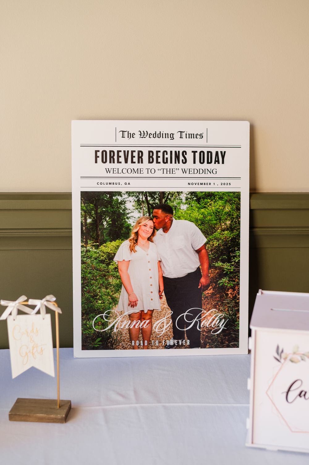 Wedding newspaper-style sign reading Forever Begins Today for Anna and Kelly, displayed at a reception table.