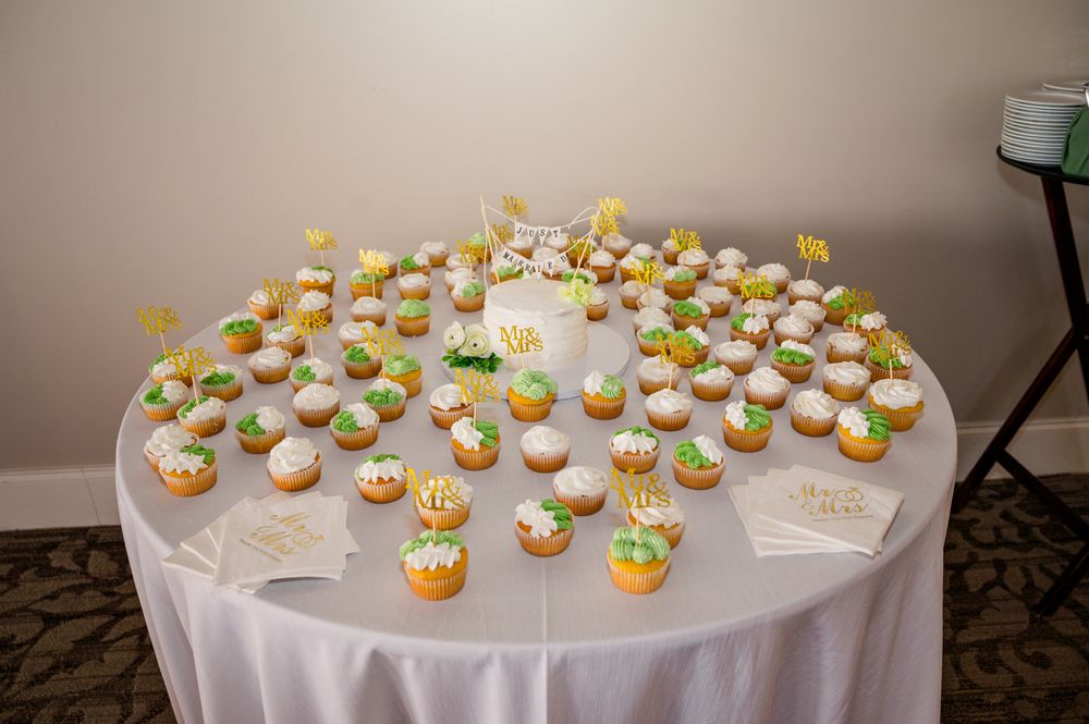 Table of decorated cupcakes with green and yellow frosting displayed at a wedding reception dessert table.
