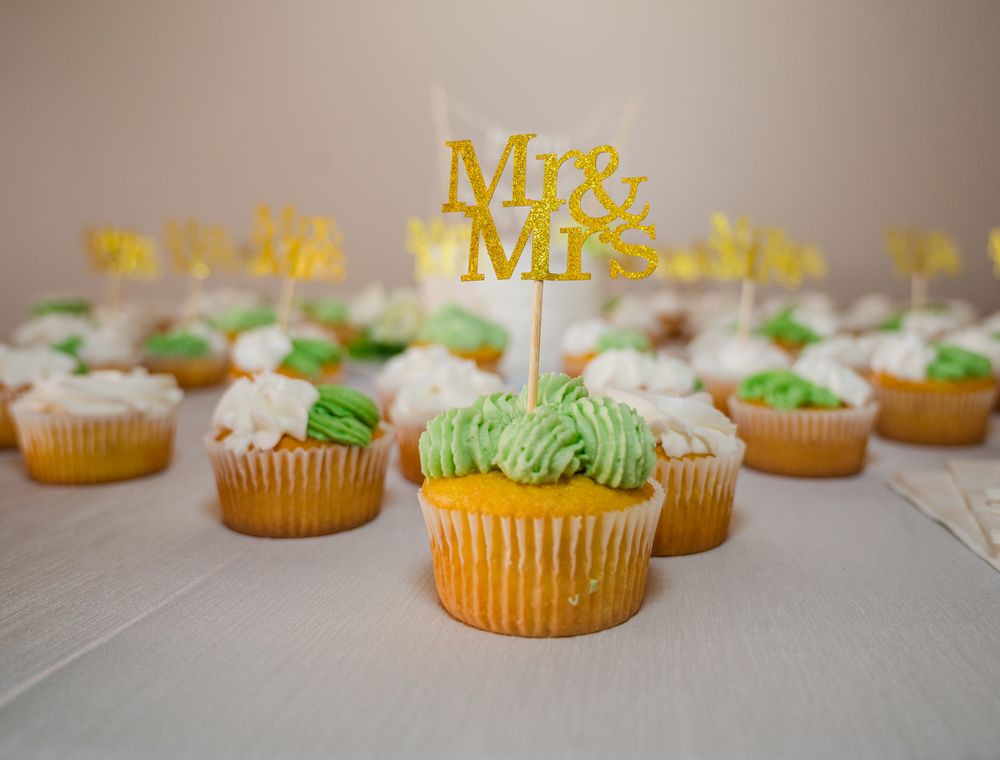 Gold Mr. & Mrs. topper on green and white frosted wedding cupcakes displayed on a table.