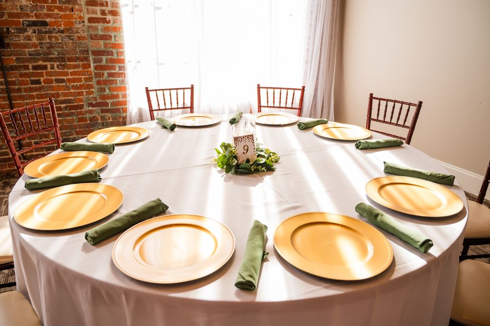 Elegant round banquet table set with gold charger plates and green napkins for a wedding reception.