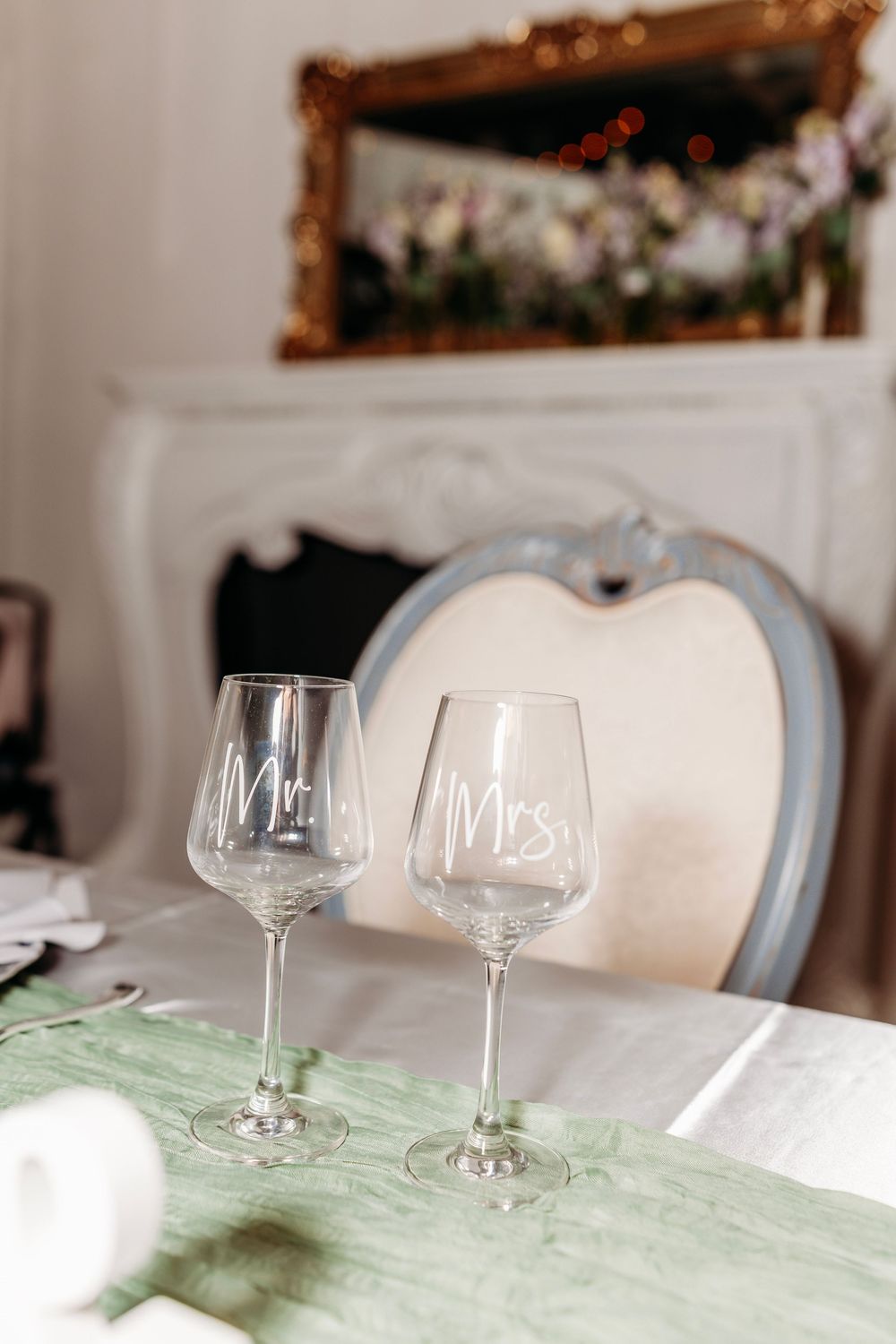 Mr. and Mrs. wine glasses on a green table runner at an elegant wedding reception with ornate mirror.