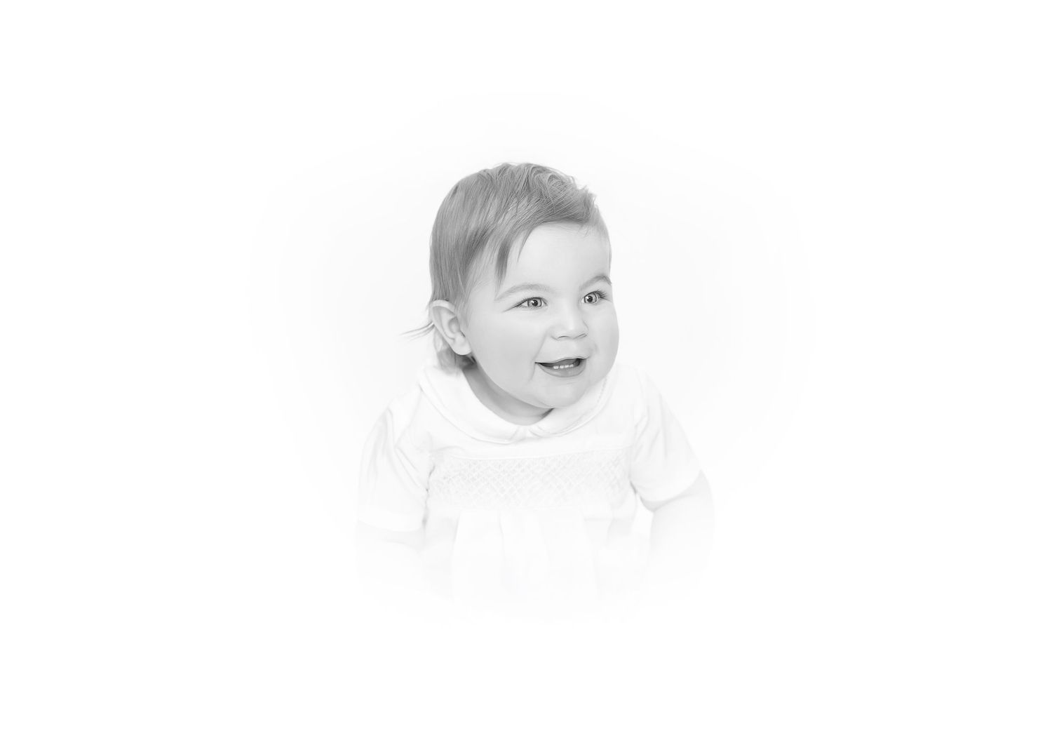 Black and white portrait of a happy smiling baby wearing a white outfit against a bright white background.