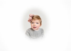 Adorable toddler girl with pink bow in hair wearing gray ruffle dress, portrait on white background.
