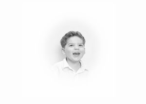 Black and white portrait of a cheerful young boy smiling and looking up, wearing a white shirt.