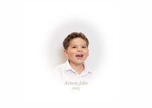 A smiling young boy named Artem John photographed in a white shirt against a soft white background in 2025.