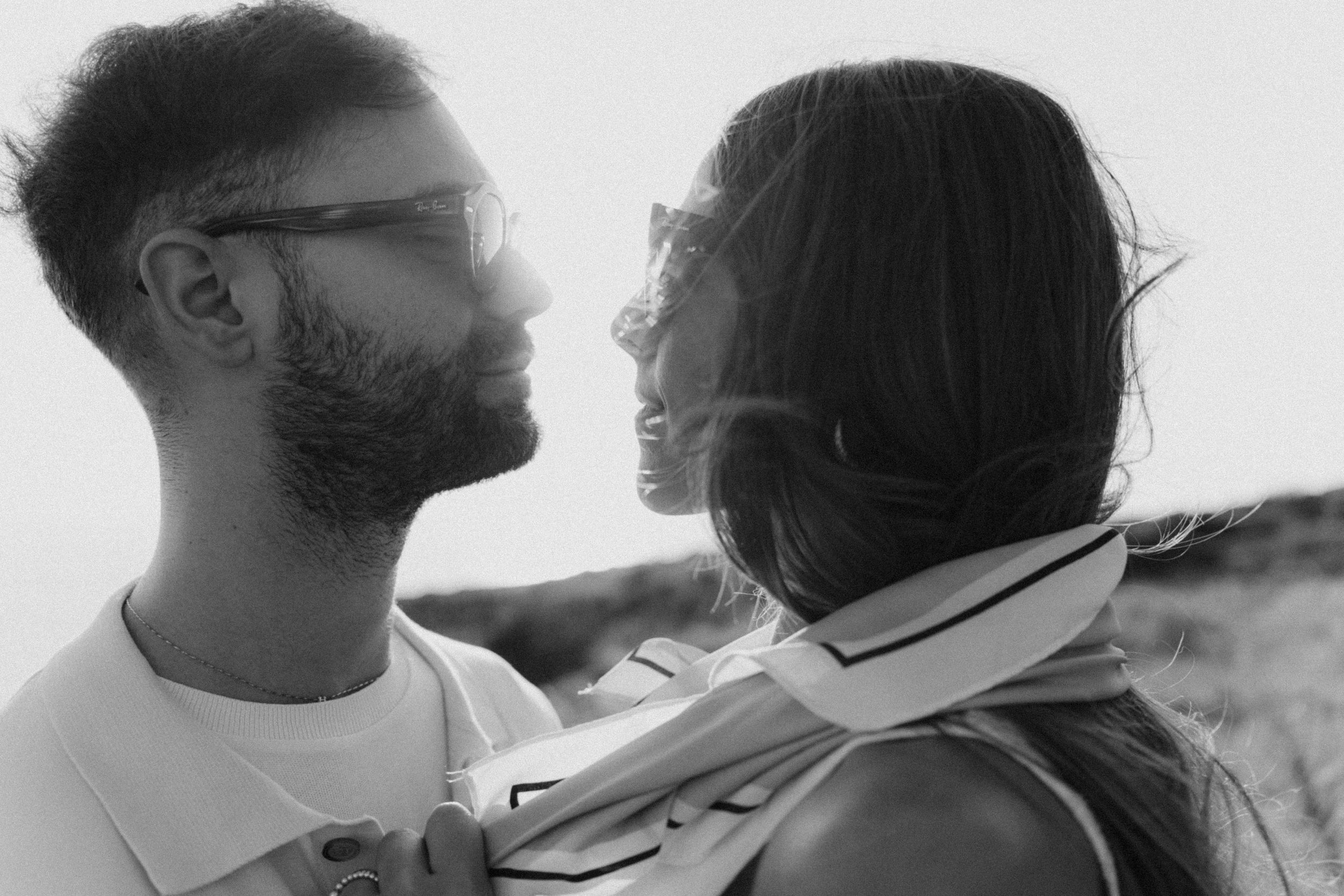 Black and white photo of a bearded man and woman gazing at each other romantically outdoors.