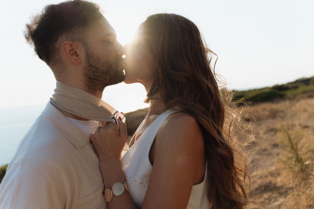 Couple sharing a tender kiss at golden hour with sunlight glowing behind them in a field.