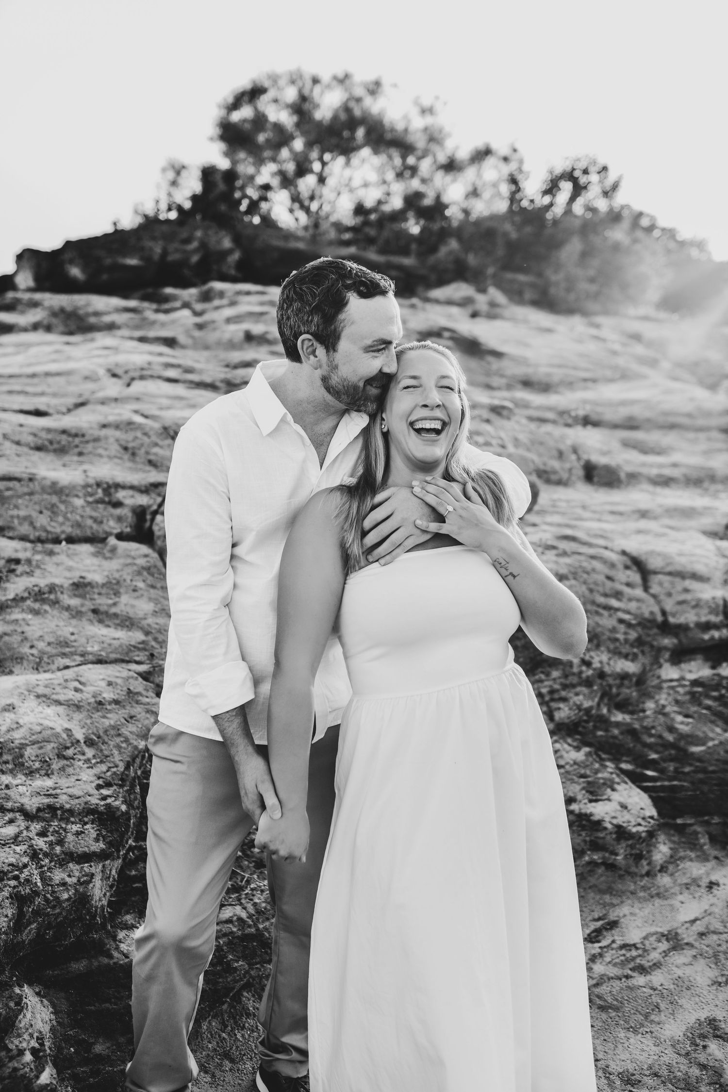 a bride to be laughs as her fiance kisses her forehead during their flower mound engagement session