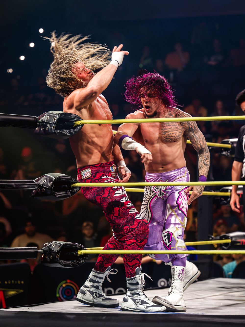 Two tattooed male wrestlers in vibrant trunks clash aggressively inside a WWE NXT wrestling ring.