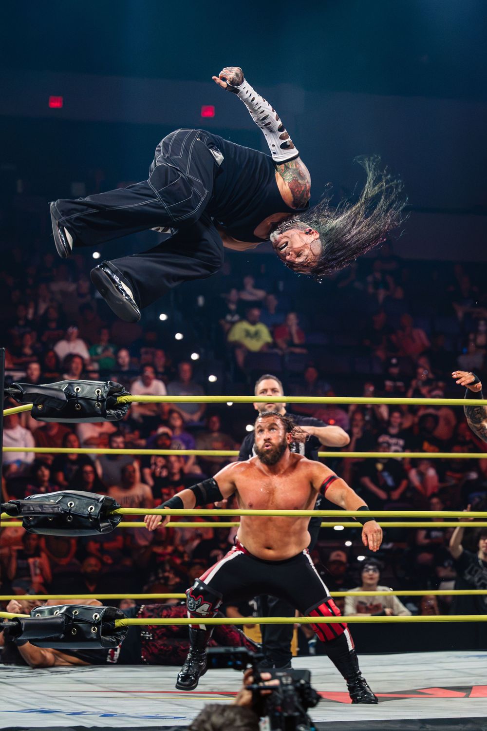 Pro wrestler performs aerial flip over opponent in WWE NXT ring match under bright arena lights.