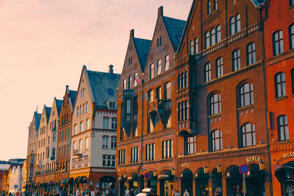 Colorful historic brick buildings with pointed gabled roofs line a busy street at sunset in Bergen, Norway.