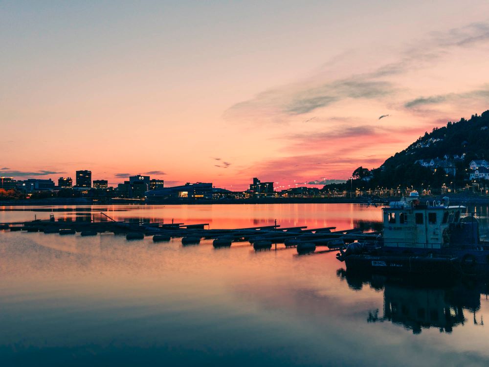 Stunning pink and orange sunset over a calm harbor with boats and city skyline reflections in Norway.