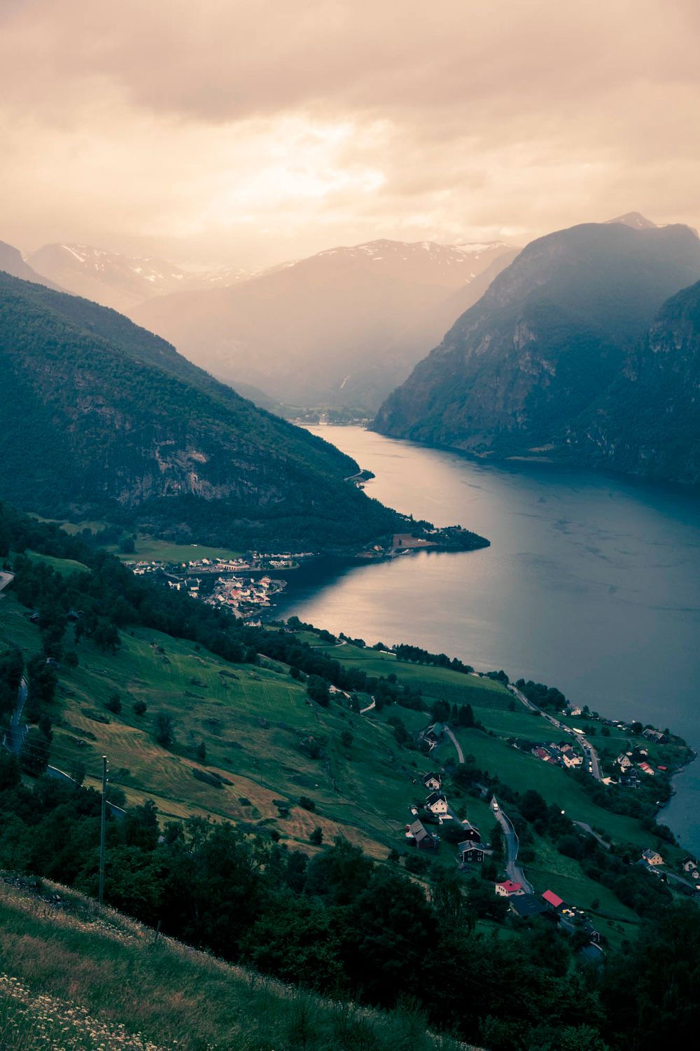 Aerial view of a Norwegian fjord village nestled between mountains at sunset with dramatic cloudy sky.