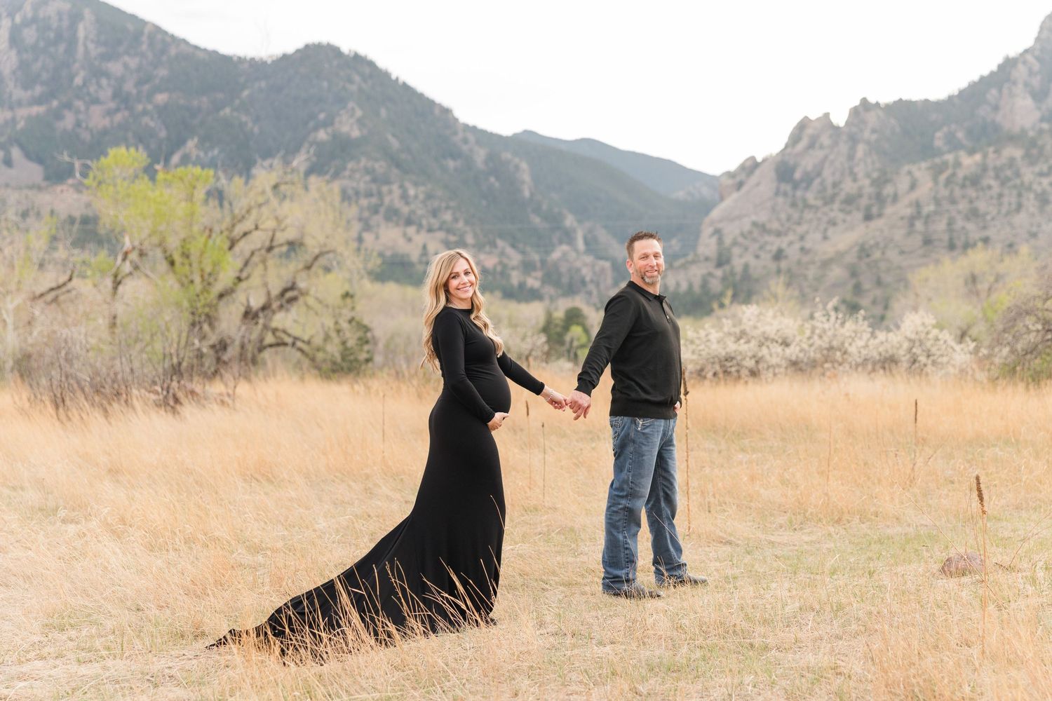Couple sitting on blanket in golden field with Rocky Mountains backdrop during maternity photo session.
