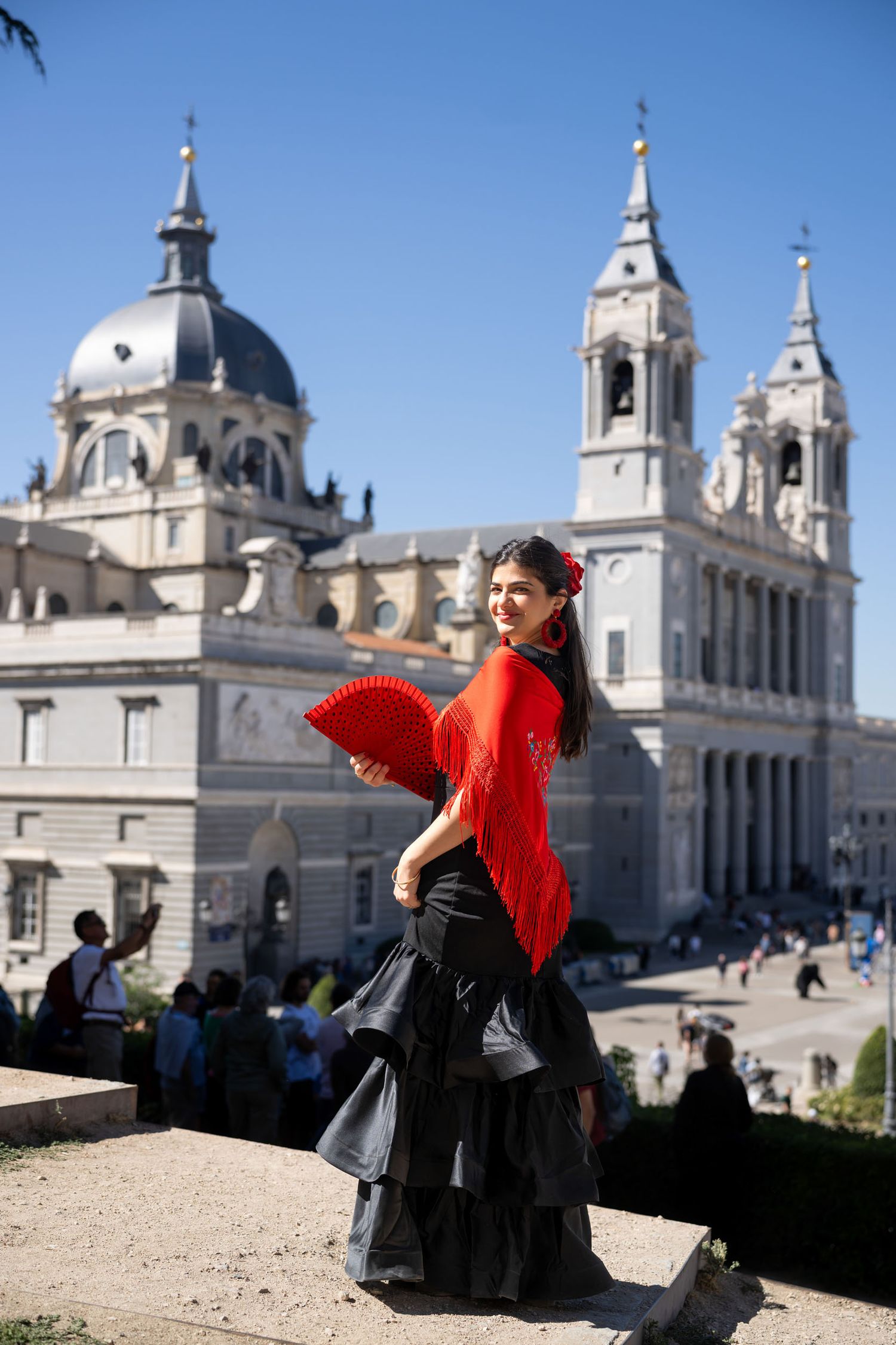 A flowing blue dress creates an ethereal silhouette against the stunning backdrop of Madrid's Almudena Cathedral at sunset.