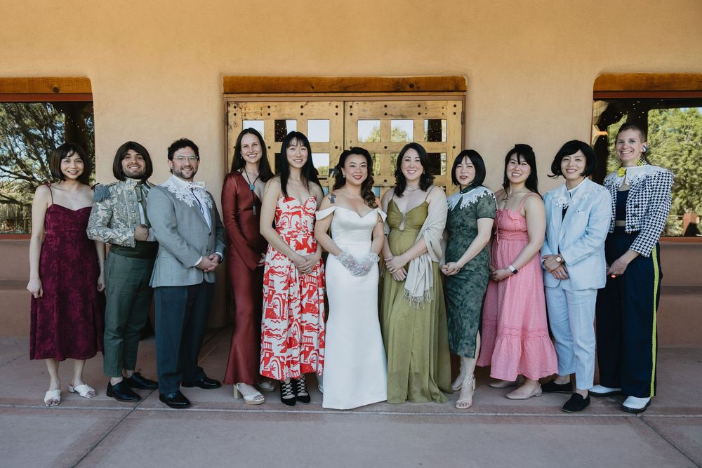 Wedding party group portrait outside adobe venue in colorful attire with bride in white gown.