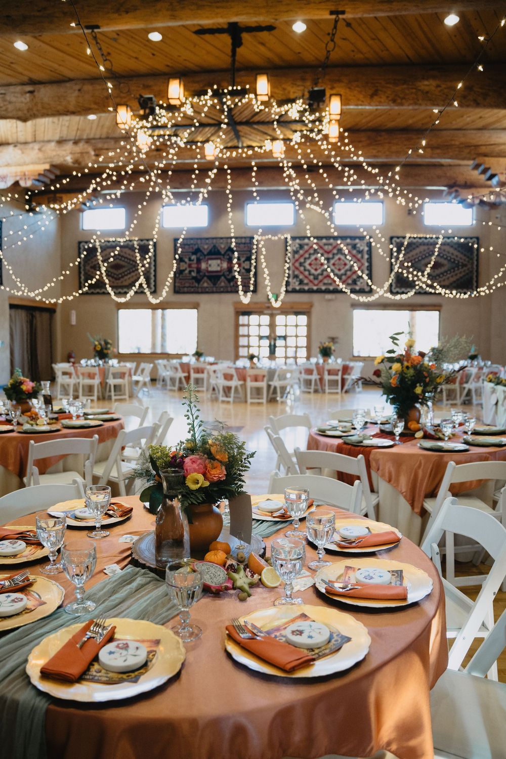 Rustic wedding venue with wooden ceiling, fairy lights, and beautifully set tables with orange linens at Nature Pointe Venue in New Mexico