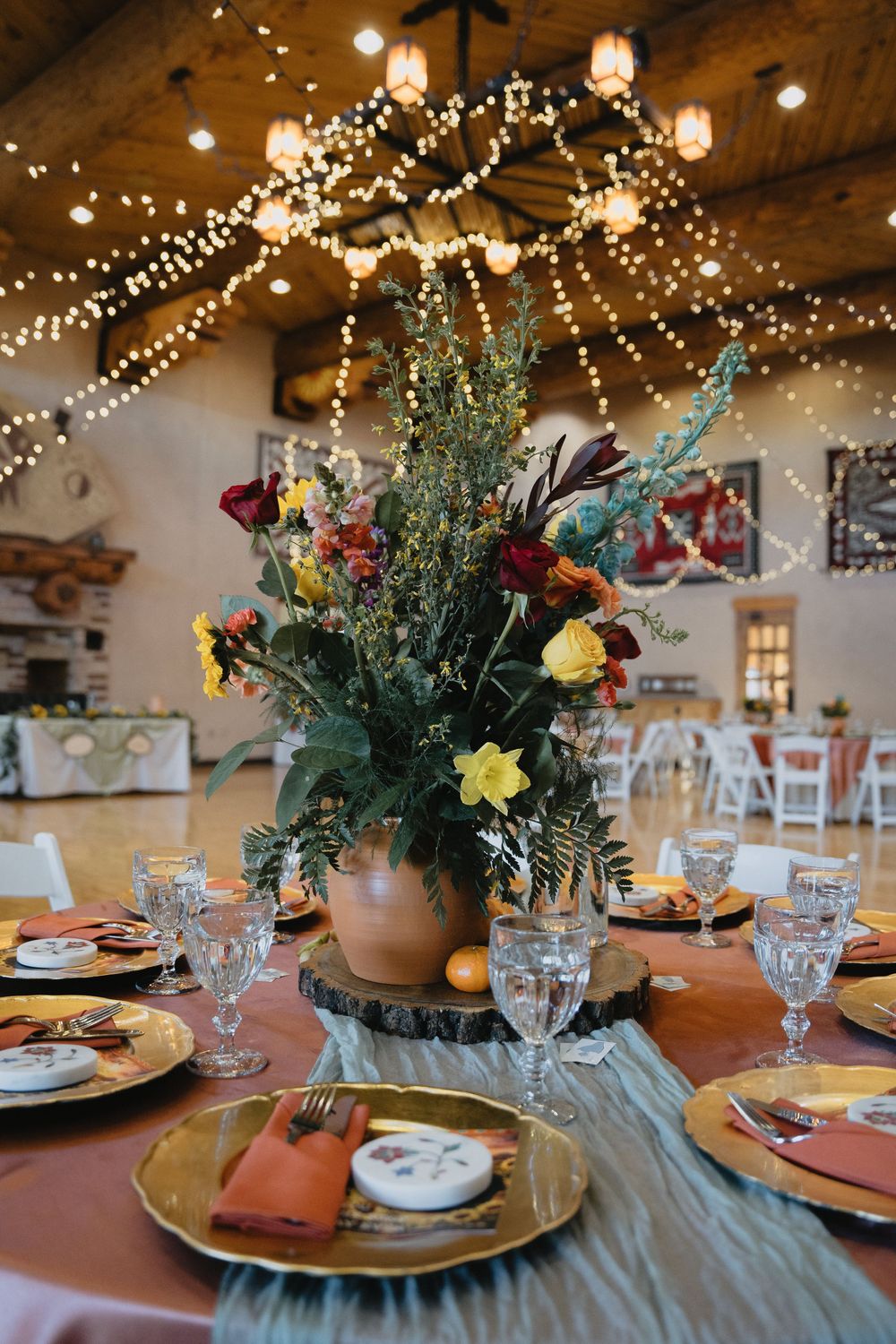 Vibrant wildflower centerpiece in terracotta pot on wood slice with gold charger plates at wedding at Nature Pointe Venue