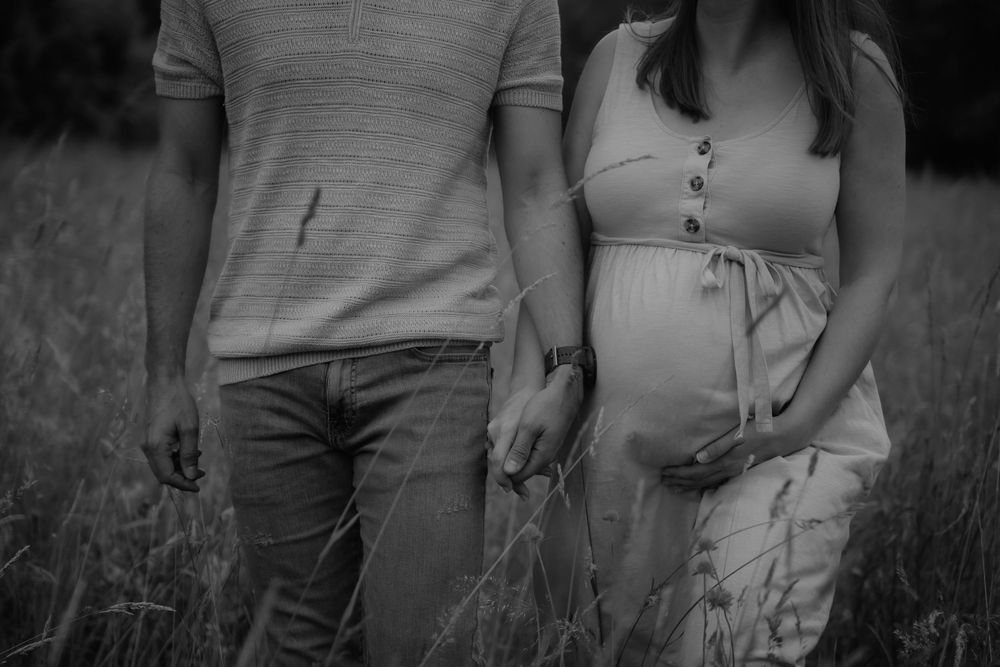 Black and white photo of a pregnant couple holding hands in a field, showcasing a maternity photoshoot.