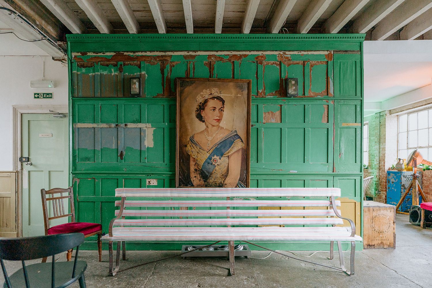 Vintage room with green paneled wall, Queen Elizabeth portrait, white bench, and red chair on concrete floor.