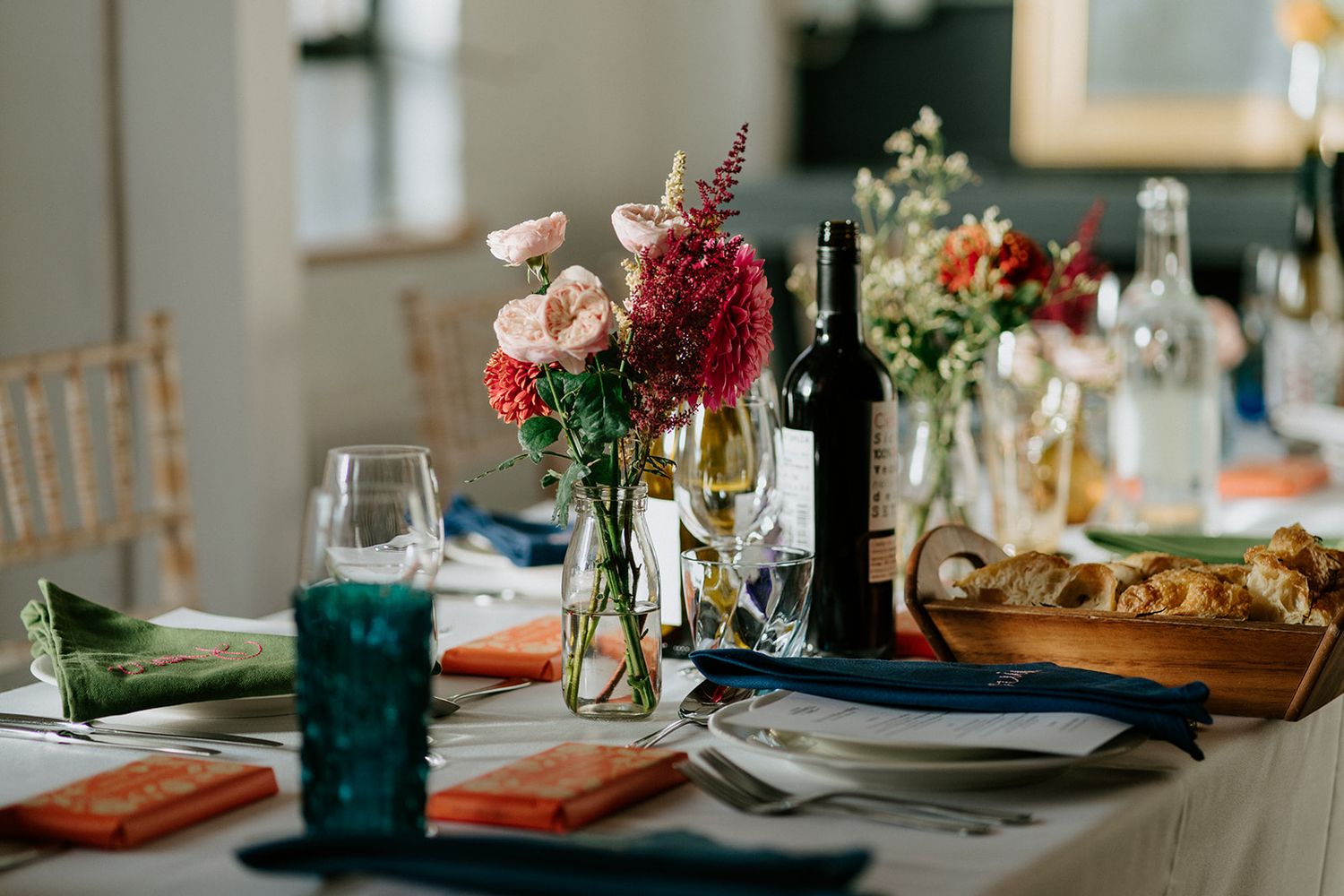 Elegant dining table set with colorful flowers, wine bottle, glassware, and vibrant napkins for a festive occasion.