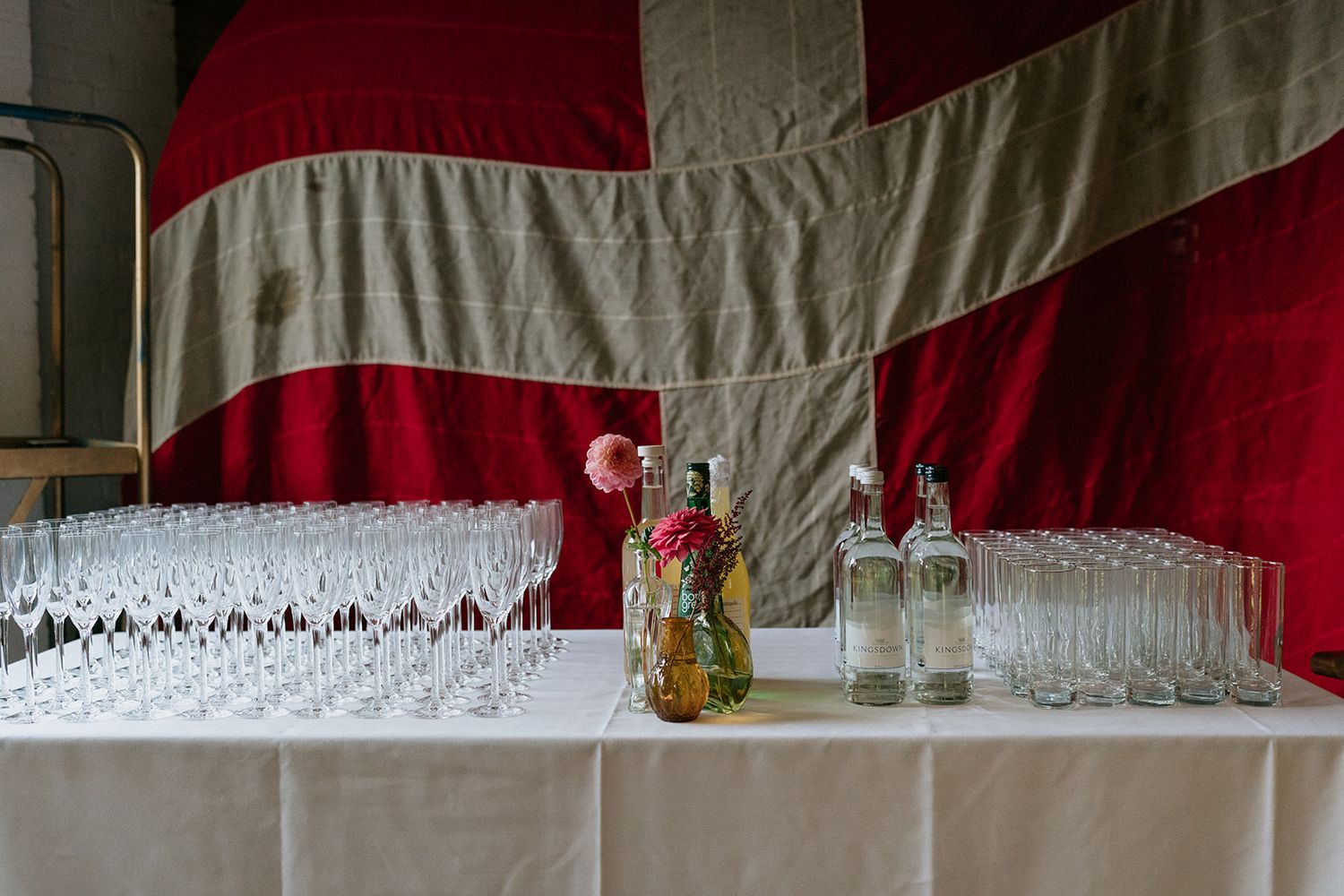 Elegant table setup with wine glasses and flowers in front of a large Danish flag.