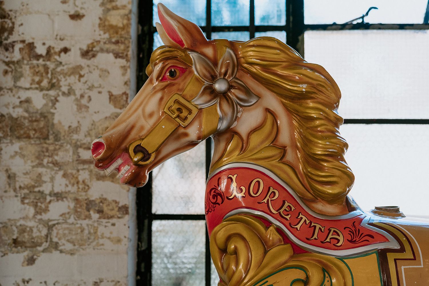 Ornate vintage carousel horse named Loretta with colorful painted details displayed indoors near a window.