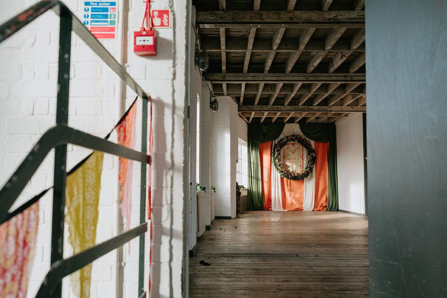Empty industrial hallway with wooden floors, exposed ceiling, and colorful fabric installation.