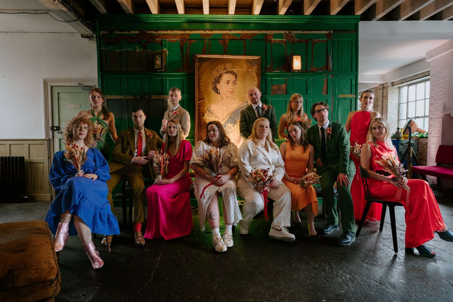 Group of elegantly dressed wedding guests pose together in a colorful, vintage-styled room.