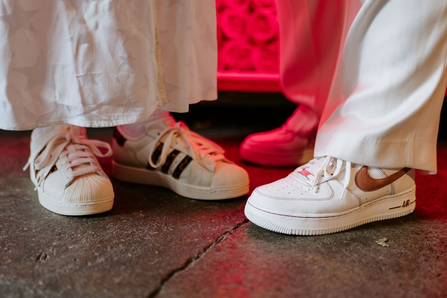 Close-up of two people wearing white Adidas and Nike sneakers on a colorful floor.