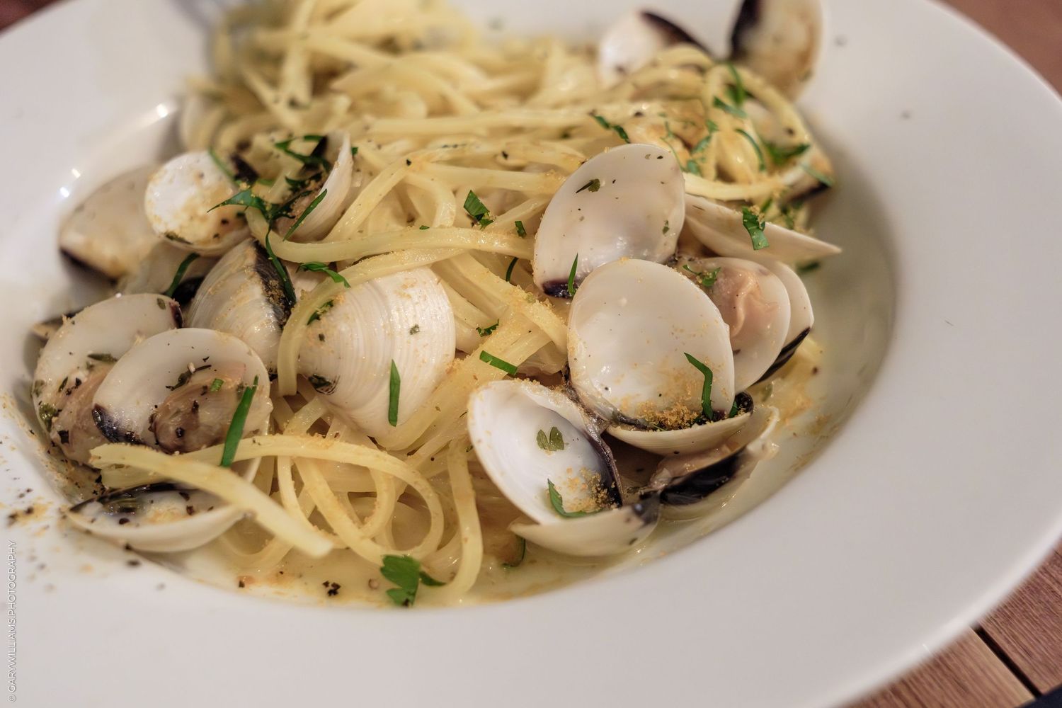 Spaghetti alle vongole with fresh clams, herbs, and olive oil served on a white plate.