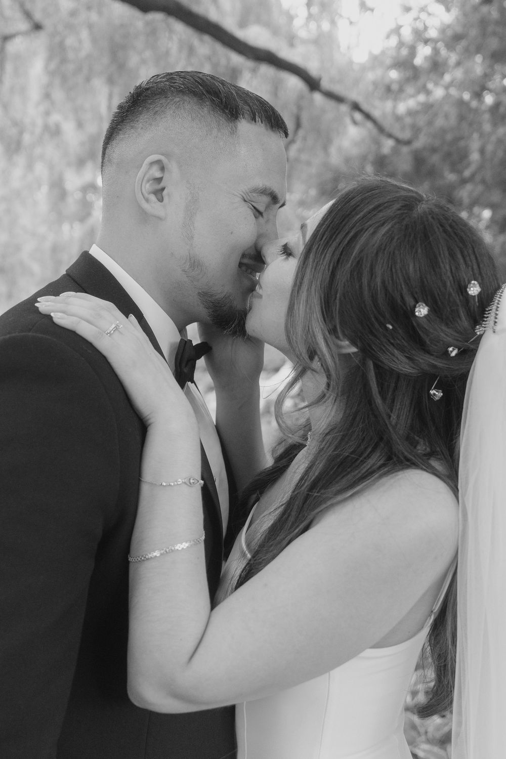 Black and white photo of a bride and groom sharing a romantic kiss on their wedding day outdoors.