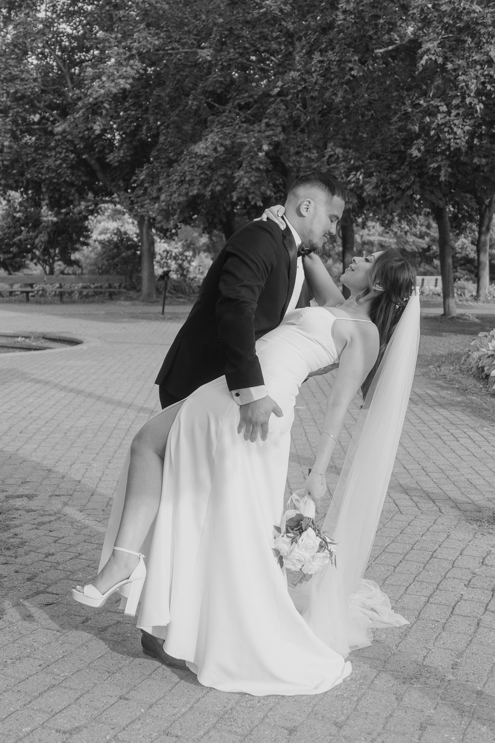 Black and white photo of groom dipping bride in a romantic kiss on a brick plaza outdoors.