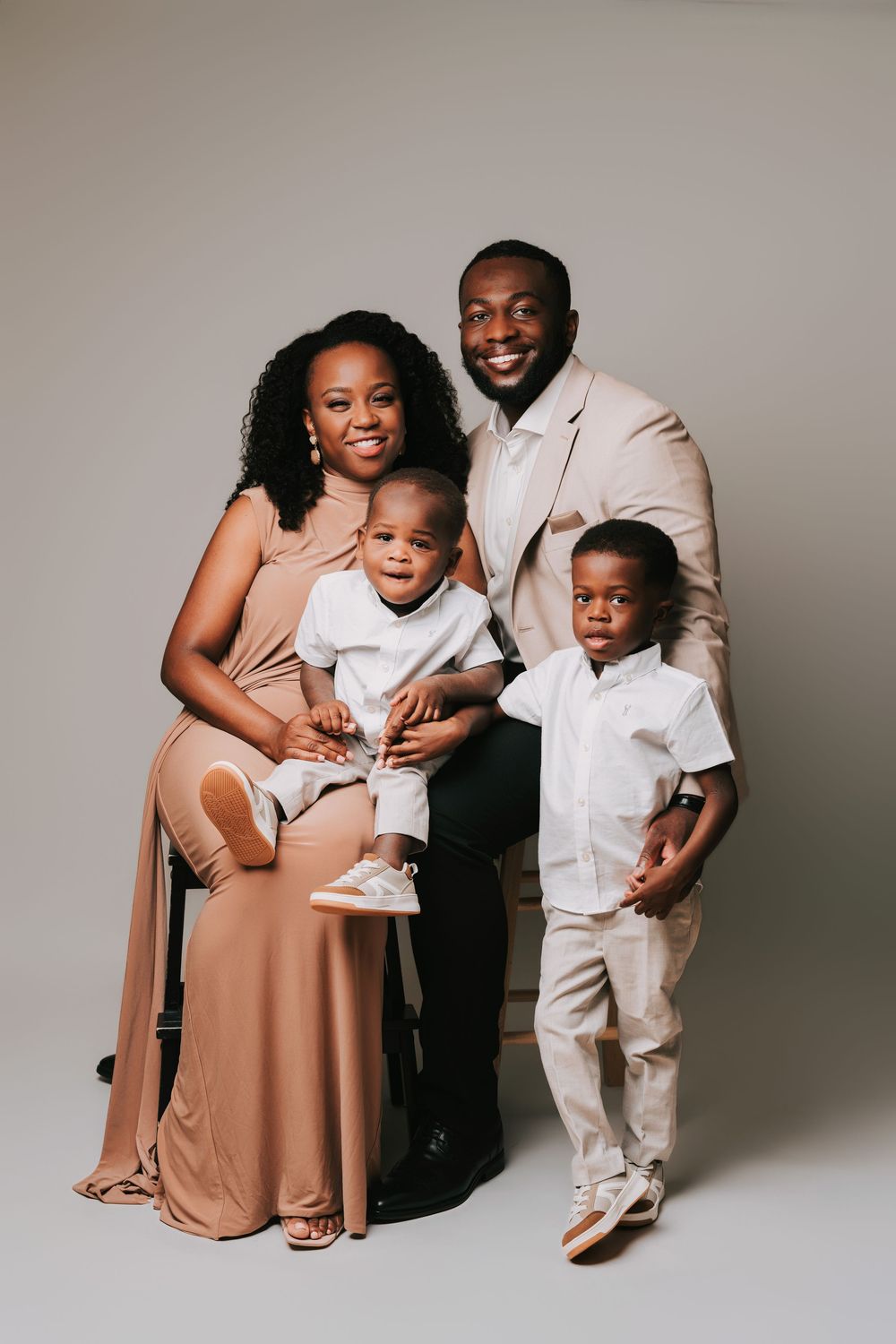 A joyful Black family of four poses together in coordinating beige outfits during a professional studio portrait session.