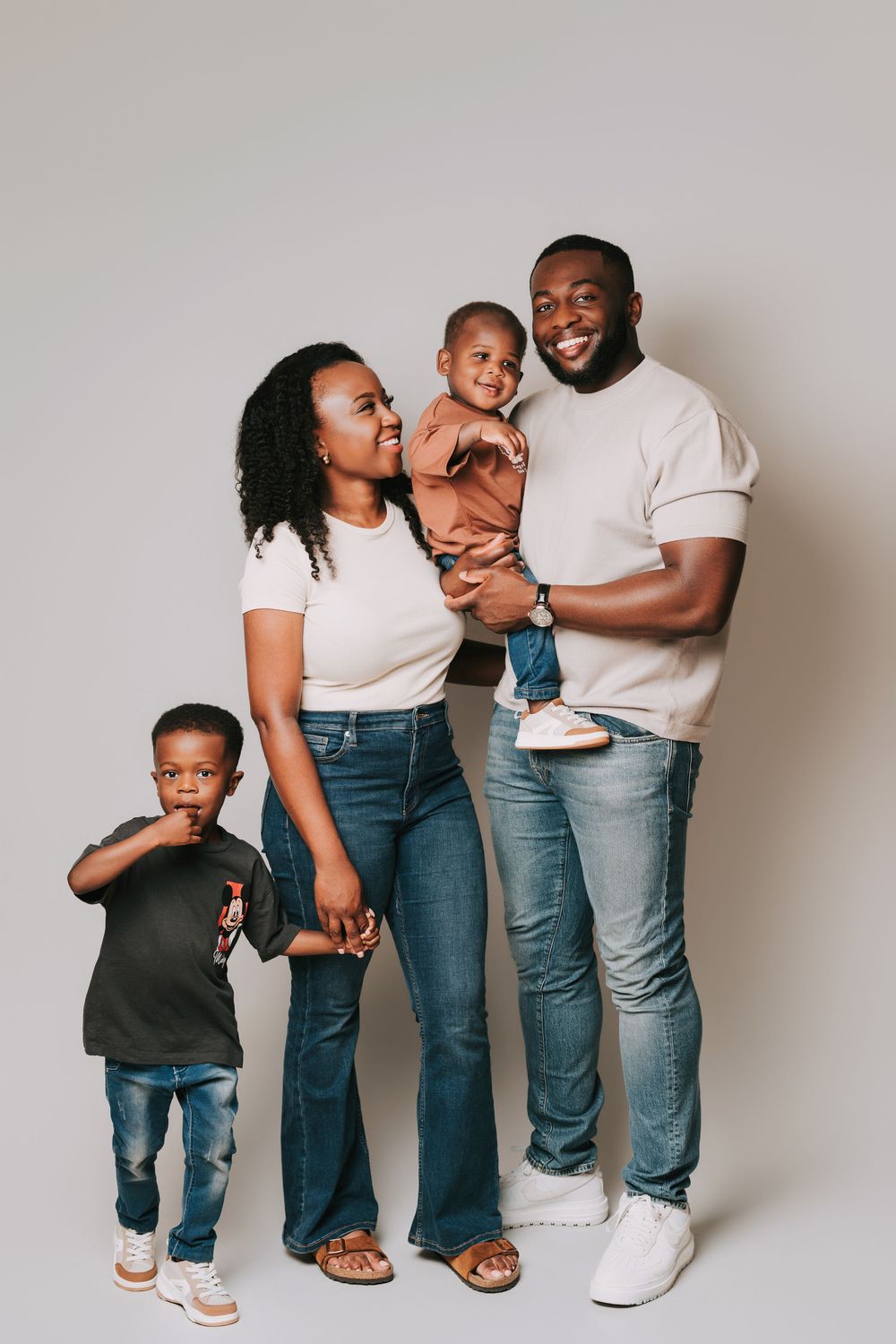 Happy Black family of four posing together in a studio, parents smiling with two young children against a gray background.