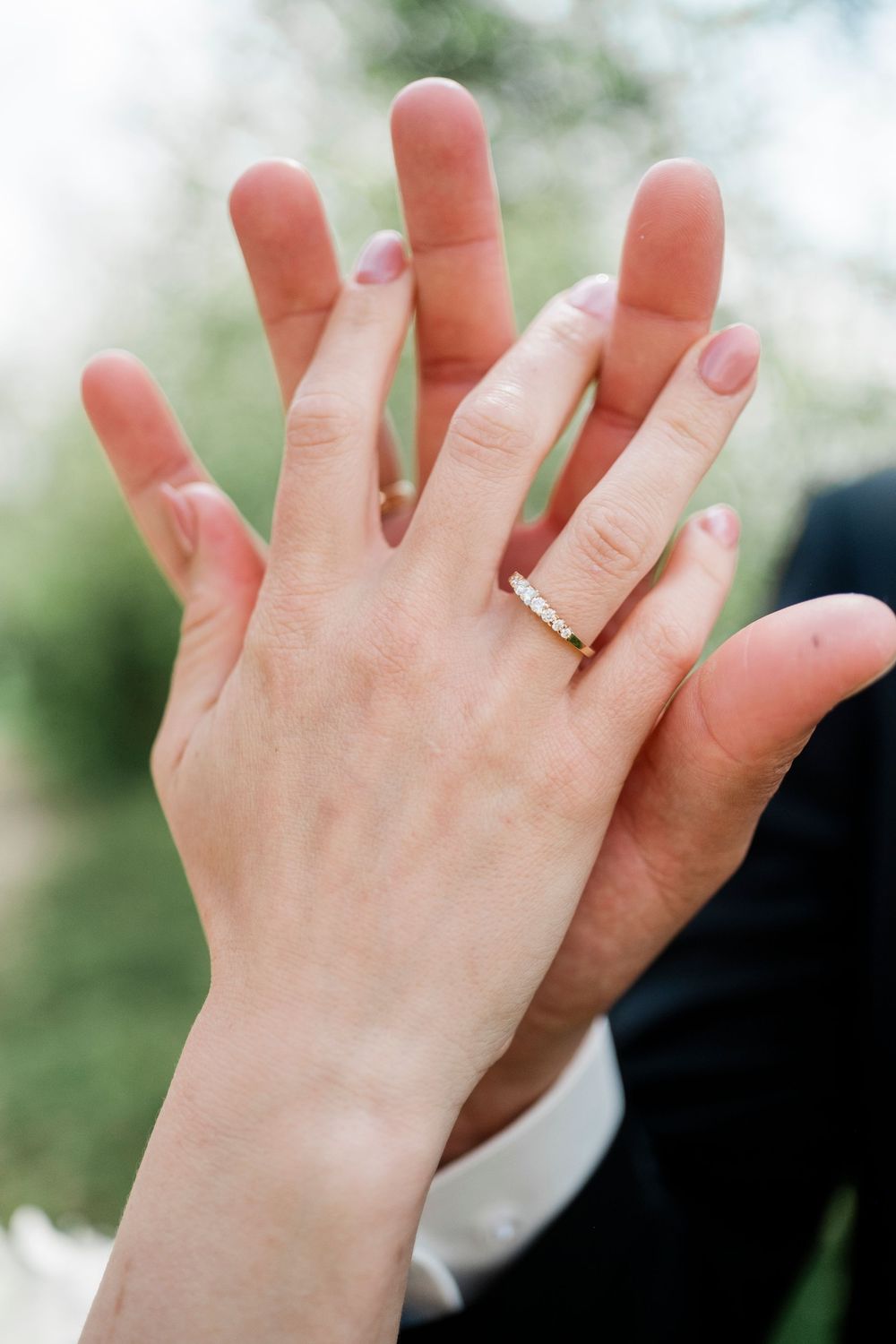 Close-up of newlyweds hands touching showing diamond wedding band ring on brides finger outdoors.